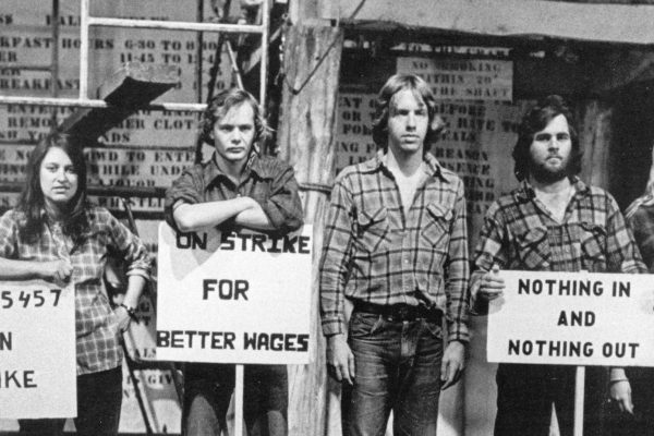 A black and white photo of 5 people with 3 strike signs in front of them. They're each wearing jeans and plaid shirts.