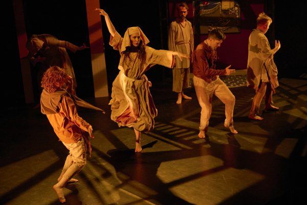 A group of young men and women dance in old-fashioned beige clothing.